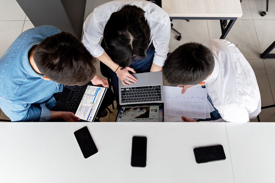 Tri kolege zajedno rade na laptopima za uredskim stolom s dokumentima